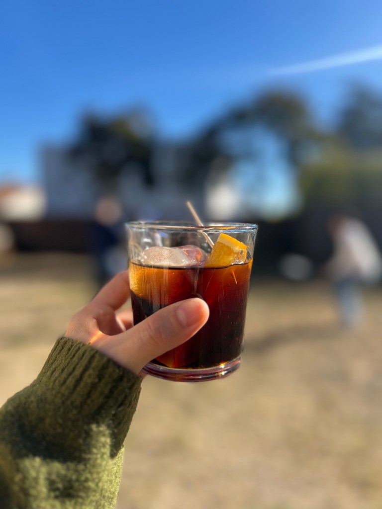 Mano sosteniendo un vaso de vermú con hielo y naranja en una terraza de Barcelona