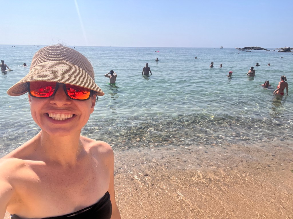 Mujer sonriente con sombrero y gafas de sol en la playa de la Costa Dorada, Tarragona, con el mar Mediterráneo de fondo
