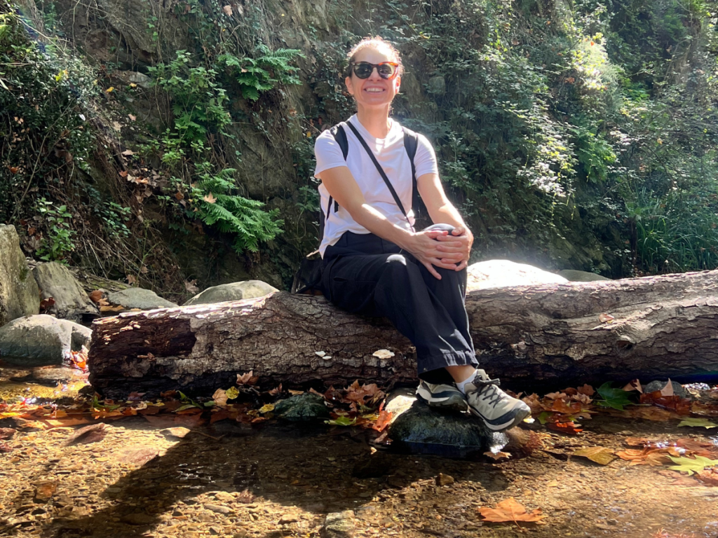 Mujer sentada sobre un tronco en el bosque con mochila y ropa de senderismo, descansando durante una ruta otoñal