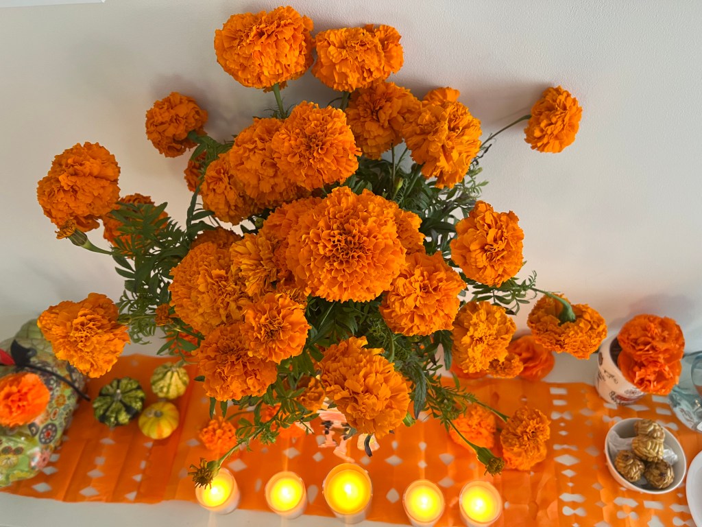 Ramo de flores de cempasúchil naranjas sobre un altar de muertos con velas y mantel tradicional.