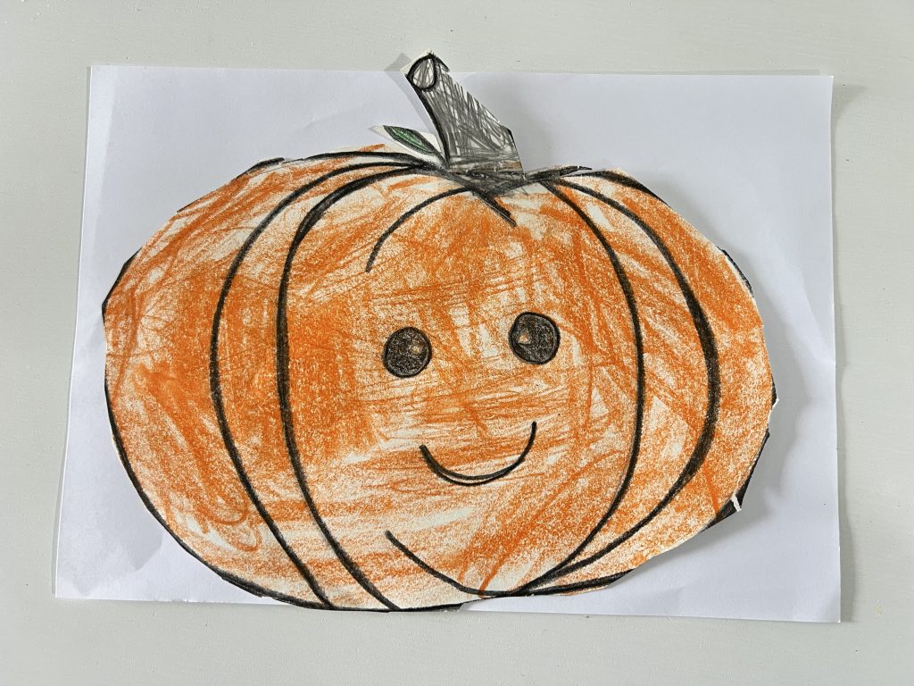 Dibujo infantil de una calabaza sonriente coloreada con tonos naranjas, hecho por un niño durante la temporada de Halloween y Día de Muertos.