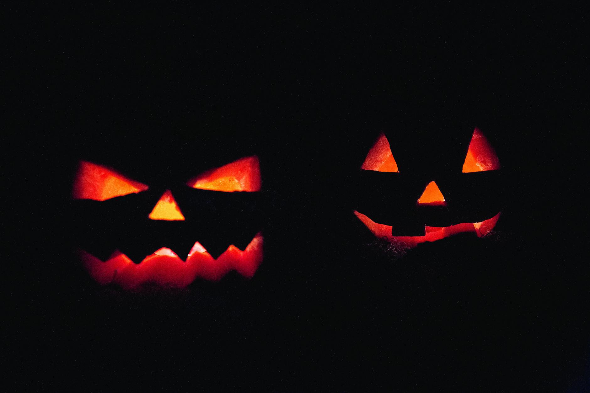 Dos calabazas talladas con caras iluminadas por dentro, típicas de Halloween, sobre fondo oscuro.